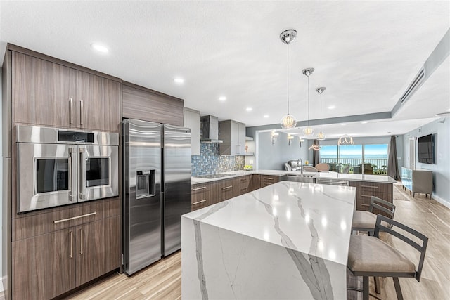 kitchen featuring appliances with stainless steel finishes, a kitchen bar, wall chimney range hood, kitchen peninsula, and a large island