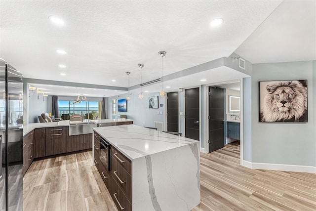 kitchen featuring light stone countertops, a spacious island, light hardwood / wood-style flooring, and dark brown cabinets