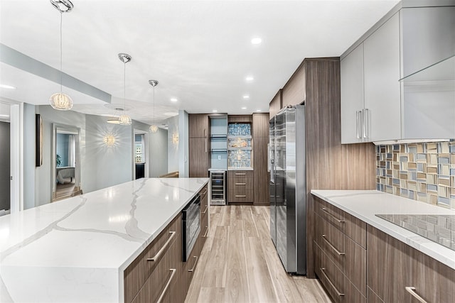 kitchen featuring stainless steel appliances, backsplash, decorative light fixtures, wine cooler, and light stone counters