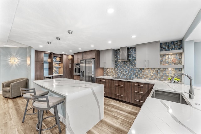 kitchen with sink, hanging light fixtures, light stone countertops, appliances with stainless steel finishes, and wall chimney exhaust hood