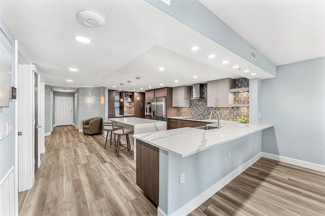 kitchen featuring decorative light fixtures, backsplash, kitchen peninsula, stainless steel fridge with ice dispenser, and wall chimney exhaust hood