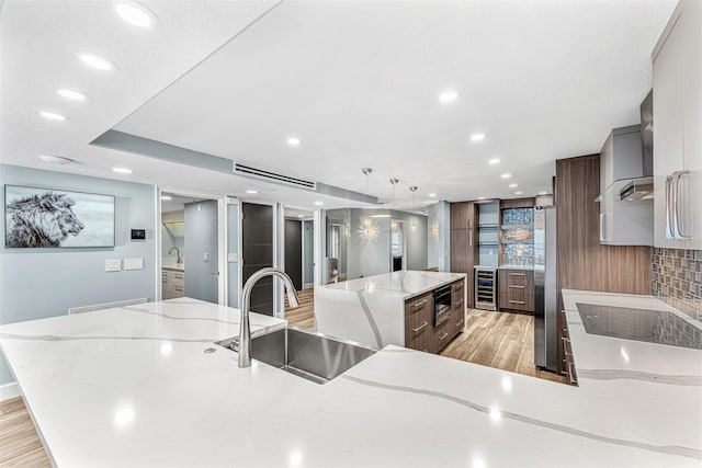 kitchen with stainless steel fridge, a large island, wine cooler, light stone counters, and sink