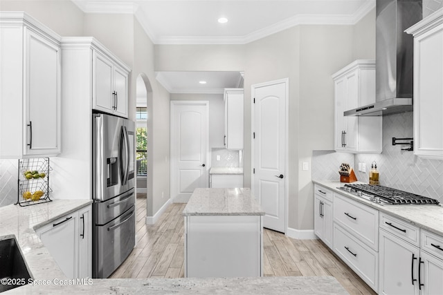 kitchen featuring wall chimney range hood, light stone countertops, white cabinets, and appliances with stainless steel finishes