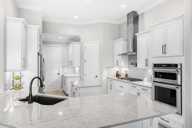 kitchen with appliances with stainless steel finishes, white cabinetry, sink, light stone counters, and wall chimney exhaust hood