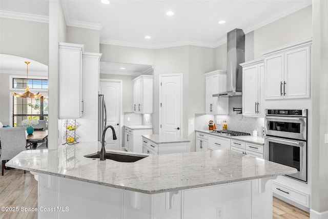 kitchen with appliances with stainless steel finishes, wall chimney exhaust hood, white cabinetry, sink, and kitchen peninsula