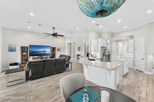 kitchen featuring stainless steel refrigerator with ice dispenser, white cabinets, light wood-type flooring, sink, and an island with sink