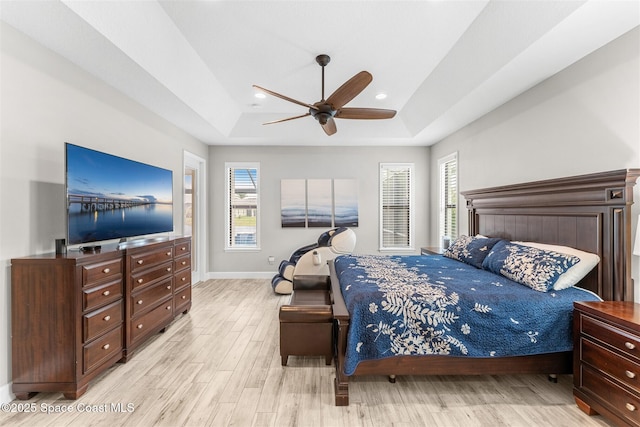 bedroom with ceiling fan, multiple windows, a raised ceiling, and light wood-type flooring