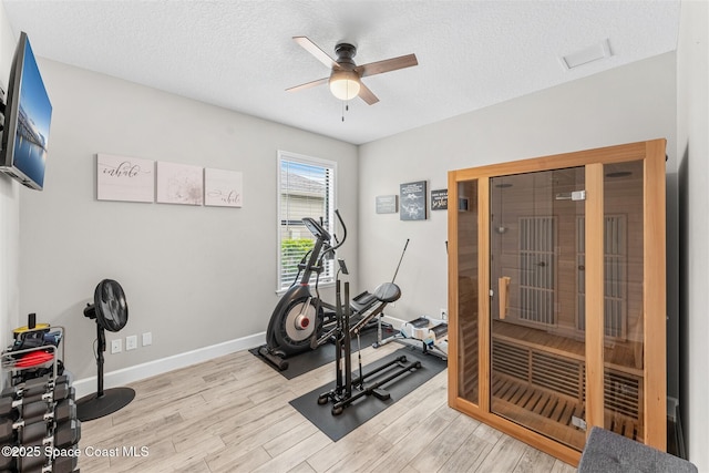 exercise room with ceiling fan, light hardwood / wood-style floors, and a textured ceiling