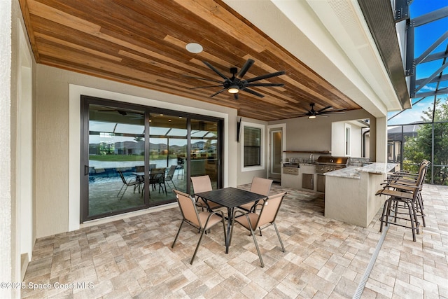 view of patio featuring a bar, ceiling fan, a water view, grilling area, and an outdoor kitchen