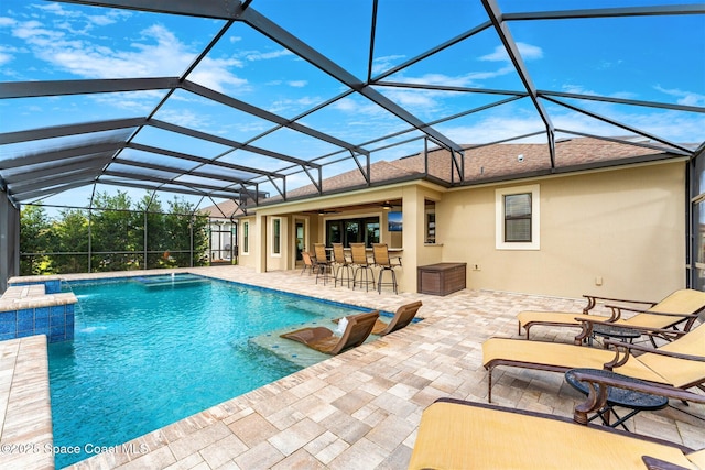 view of pool with glass enclosure, ceiling fan, exterior bar, pool water feature, and a patio