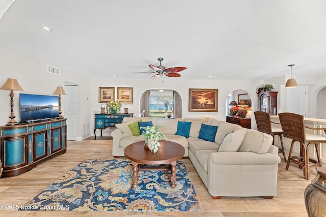 living area with arched walkways, recessed lighting, visible vents, light wood-style flooring, and a ceiling fan