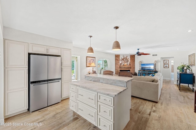 kitchen with light wood-style floors, hanging light fixtures, a brick fireplace, freestanding refrigerator, and a center island