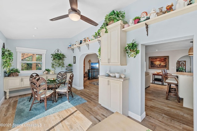 dining room featuring light wood-type flooring, baseboards, arched walkways, and a ceiling fan