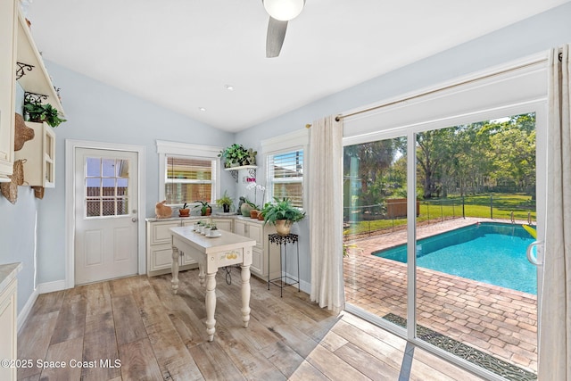 doorway to outside with light wood-style floors, baseboards, vaulted ceiling, and a ceiling fan