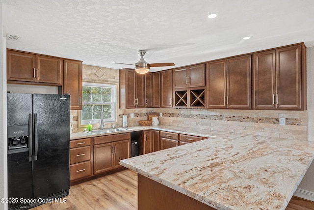 kitchen with visible vents, a sink, light wood-type flooring, a peninsula, and black fridge