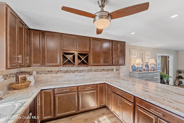 kitchen with tasteful backsplash, a ceiling fan, light wood-style flooring, and light stone countertops