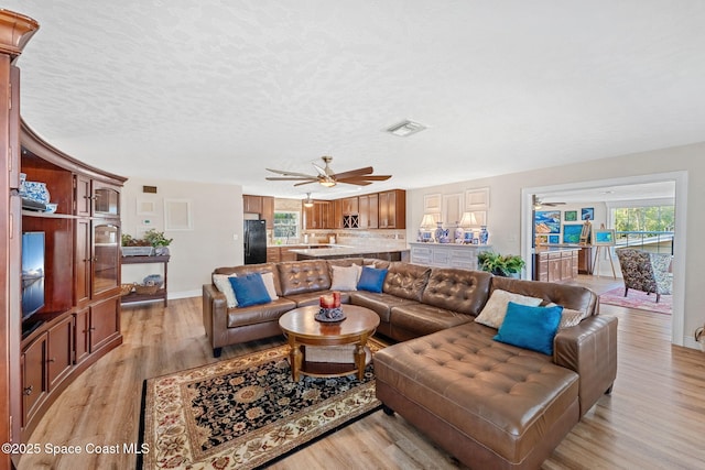 living room featuring a textured ceiling, ceiling fan, light wood-style flooring, visible vents, and baseboards