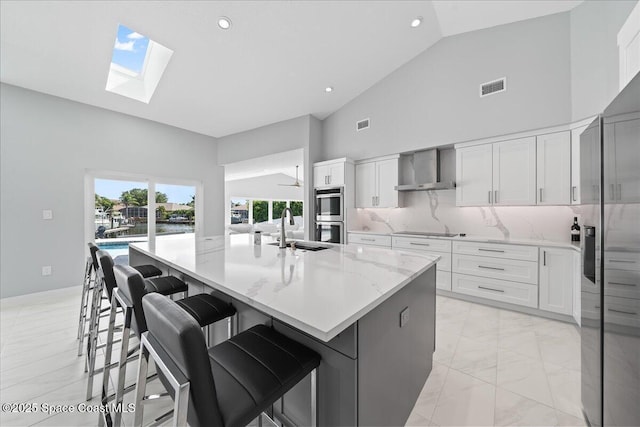 kitchen featuring white cabinetry, wall chimney range hood, sink, a large island, and black electric cooktop