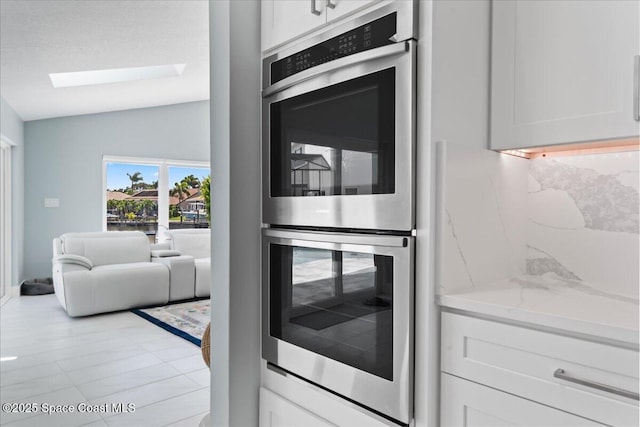 kitchen with light stone countertops, stainless steel double oven, lofted ceiling with skylight, and white cabinetry