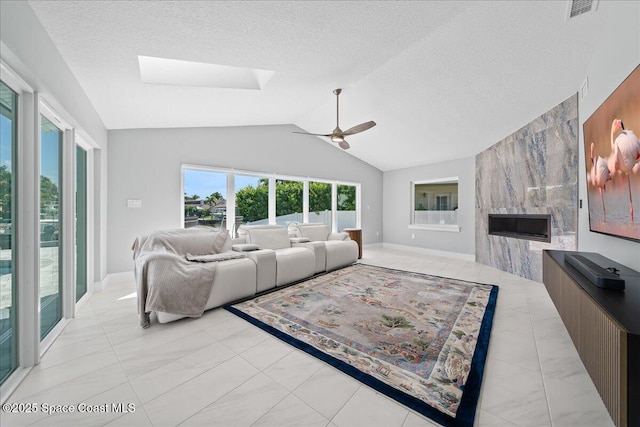 living room with a textured ceiling, ceiling fan, a large fireplace, and vaulted ceiling with skylight