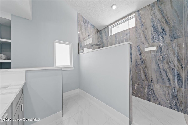 bathroom featuring a textured ceiling, a wealth of natural light, tiled shower, and vanity