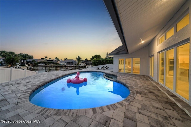 pool at dusk featuring a water view and a patio