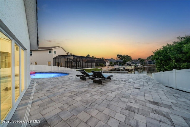 pool at dusk featuring a patio area, a lanai, and a water view