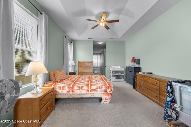 bedroom with light colored carpet, ceiling fan, and a tray ceiling