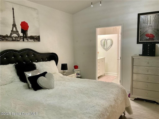 bedroom with light hardwood / wood-style flooring, connected bathroom, and vaulted ceiling