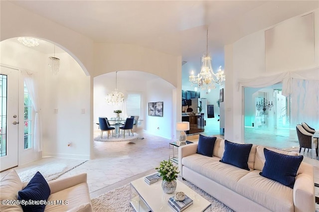 living area with a towering ceiling, marble finish floor, arched walkways, and a notable chandelier