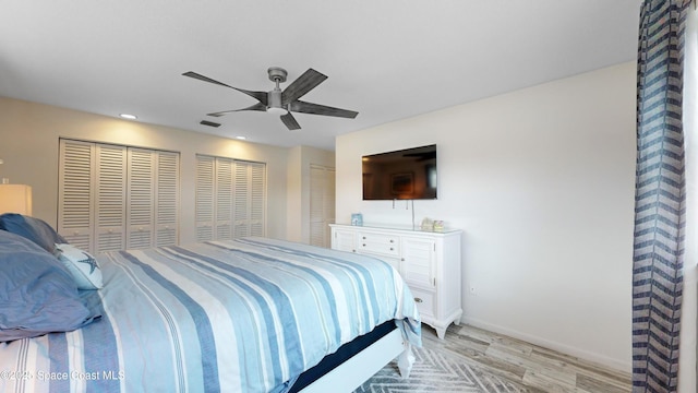 bedroom featuring ceiling fan, two closets, and light hardwood / wood-style floors