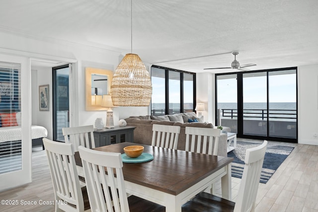 dining space featuring ceiling fan with notable chandelier, light wood-type flooring, floor to ceiling windows, and a water view