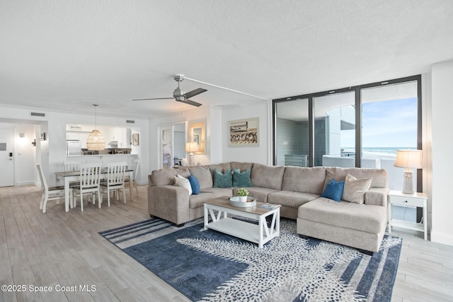 living room with ceiling fan, light hardwood / wood-style flooring, a textured ceiling, and floor to ceiling windows