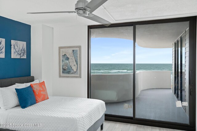 bedroom featuring ceiling fan, light wood-type flooring, a water view, and a view of the beach