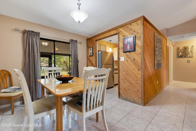 tiled dining area featuring lofted ceiling, wood walls, and a textured ceiling