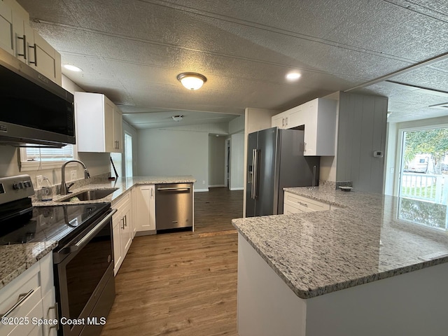 kitchen featuring appliances with stainless steel finishes, light stone countertops, kitchen peninsula, white cabinets, and sink