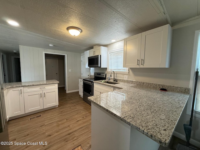 kitchen featuring light stone counters, kitchen peninsula, white cabinets, appliances with stainless steel finishes, and sink