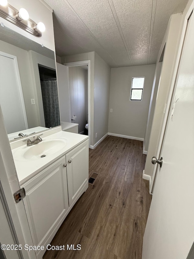 bathroom featuring toilet, hardwood / wood-style flooring, a textured ceiling, curtained shower, and vanity