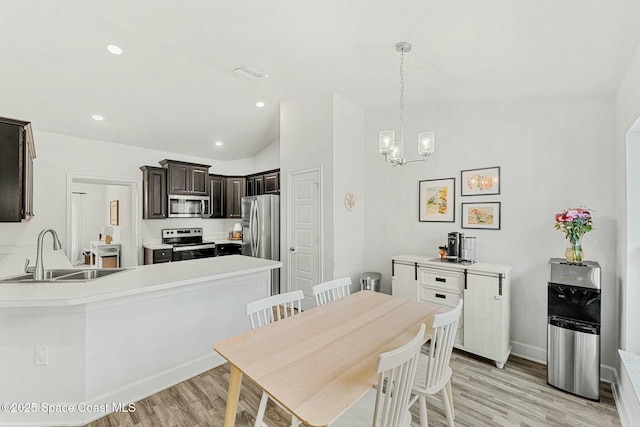 dining room with an inviting chandelier, lofted ceiling, sink, and light wood-type flooring