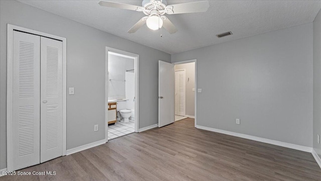 unfurnished bedroom featuring ceiling fan, light hardwood / wood-style flooring, connected bathroom, a textured ceiling, and a closet