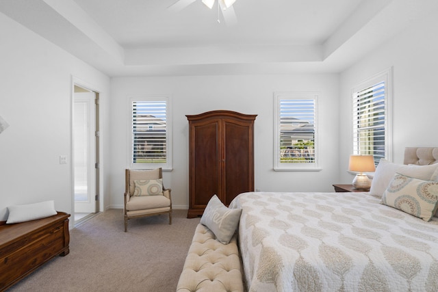 bedroom featuring ceiling fan, light carpet, and a tray ceiling