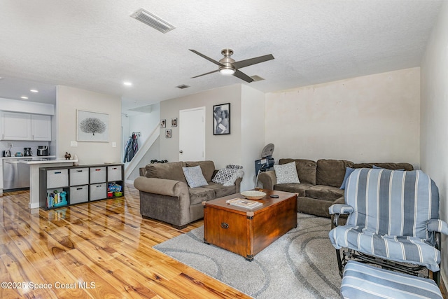 living room with ceiling fan, a textured ceiling, and light hardwood / wood-style floors