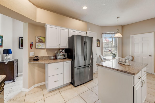 kitchen with decorative light fixtures, white cabinetry, light tile patterned flooring, stainless steel refrigerator, and a kitchen island