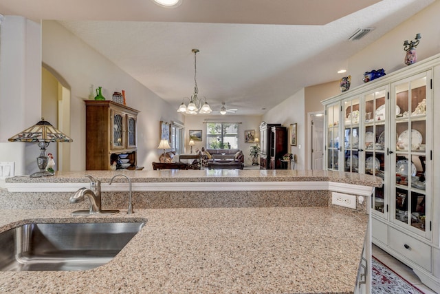 kitchen with sink, hanging light fixtures, light stone counters, and ceiling fan with notable chandelier