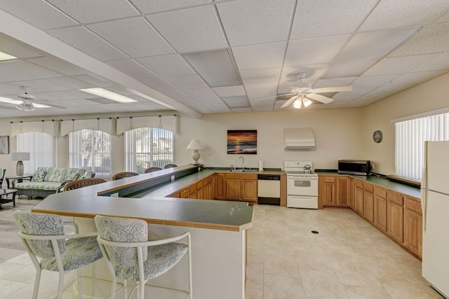 kitchen with white appliances, a kitchen breakfast bar, a paneled ceiling, kitchen peninsula, and sink