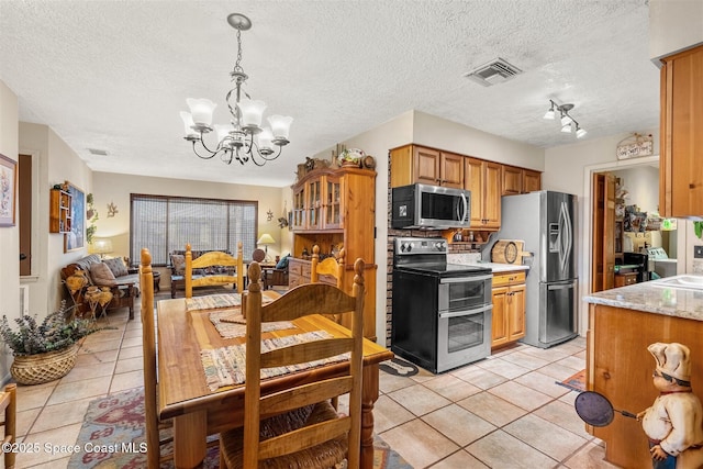 kitchen with pendant lighting, light tile patterned floors, appliances with stainless steel finishes, a notable chandelier, and light stone countertops