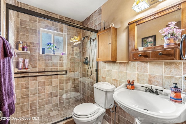 bathroom with toilet, sink, tile walls, and a shower with shower door