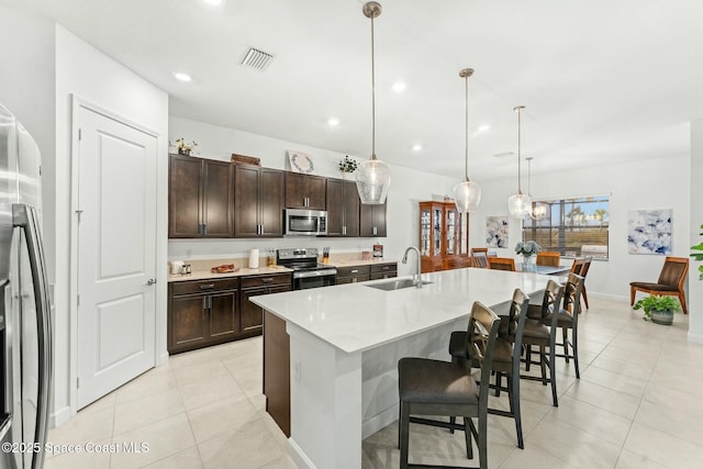 kitchen featuring pendant lighting, sink, dark brown cabinetry, an island with sink, and stainless steel appliances