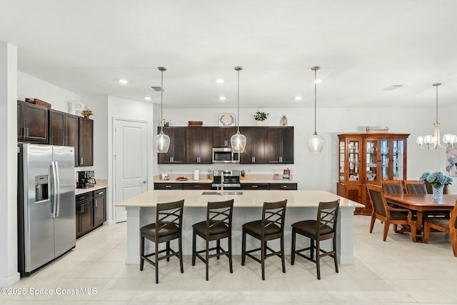 kitchen with a center island with sink, a breakfast bar area, appliances with stainless steel finishes, pendant lighting, and dark brown cabinetry