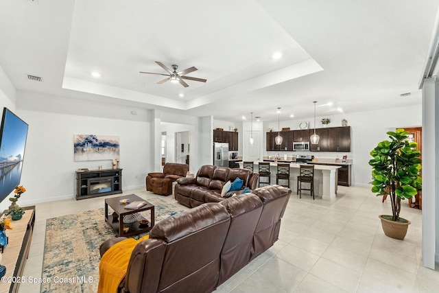 tiled living room featuring ceiling fan and a tray ceiling